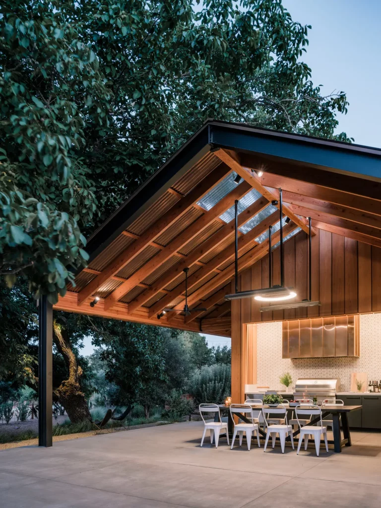 As dusk settles, the outdoor kitchen and dining space transforms into an inviting spot where culinary delights and ambiance meet.